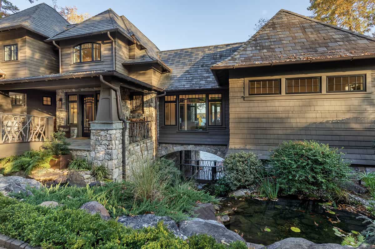Craftsman-style lake house exterior with cedar shake siding, slate roof, stone columns, and koi pond