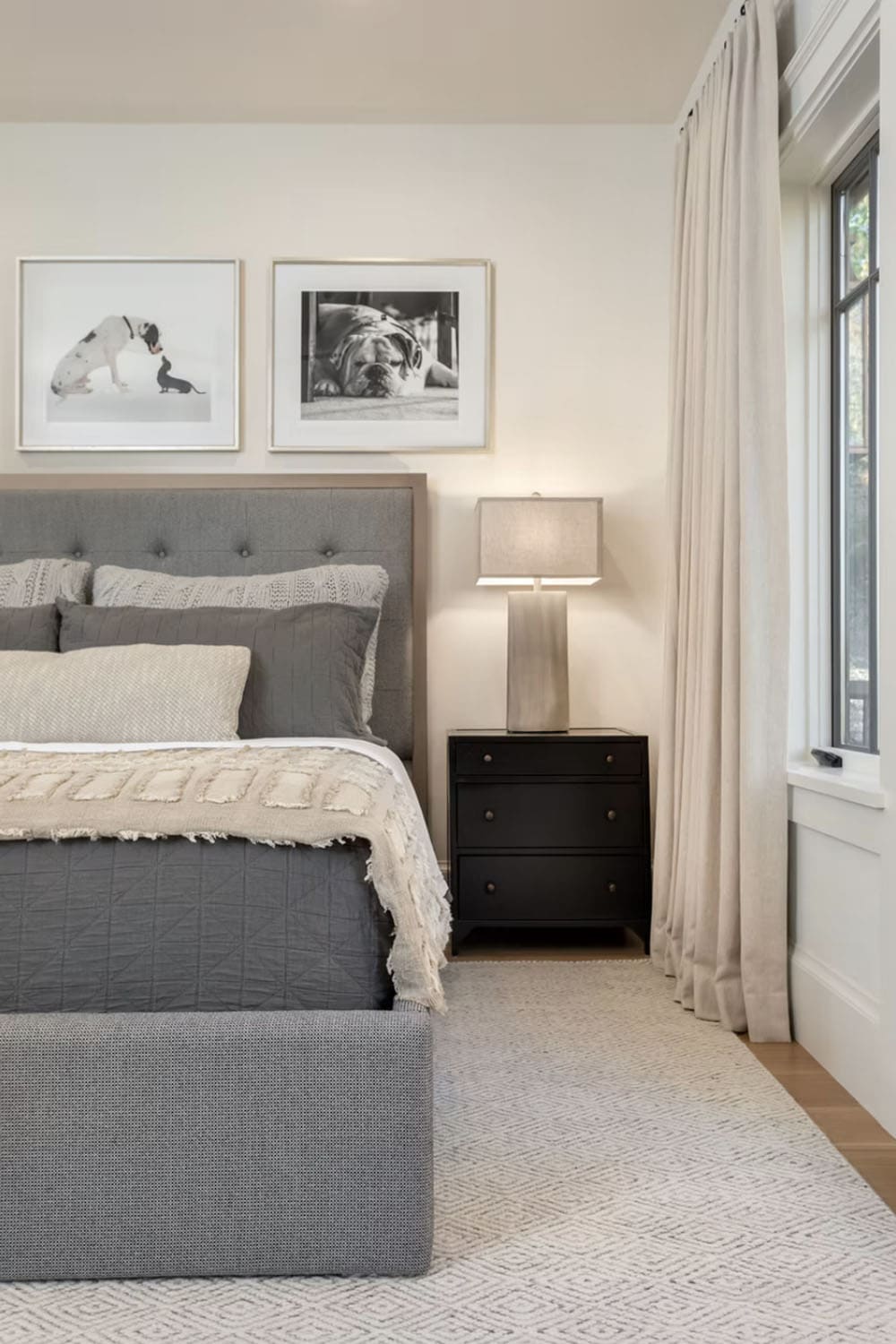 Guest bedroom with gray tufted headboard, black nightstand, and black-and-white dog photography above the bed