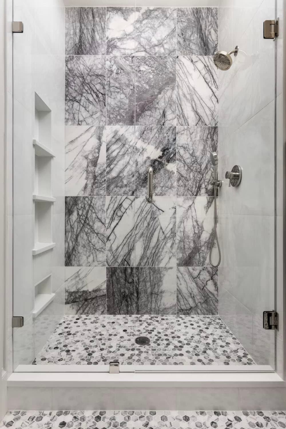 Glass-enclosed shower with dramatic gray-veined marble tile walls and hexagonal mosaic floor