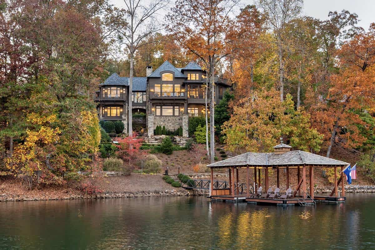 Multi-story lake house viewed from the water surrounded by autumn foliage with a covered dock