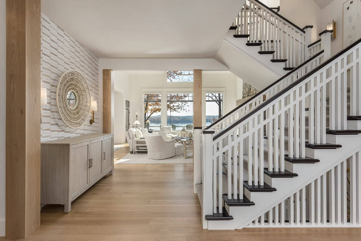 Open foyer with white staircase, light oak floors, textured stone accent wall, and woven sunburst mirror