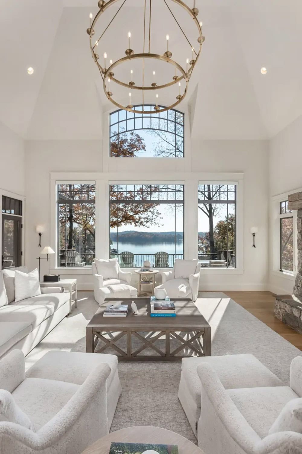 Sun-drenched lakefront living room with vaulted ceiling, brass ring chandelier, and wall of arched windows