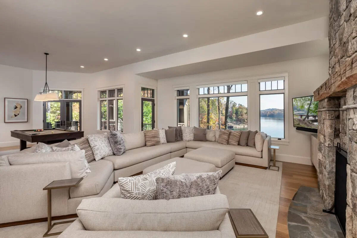 Casual family room with large sectional, stone fireplace, and panoramic lake views through grid windows