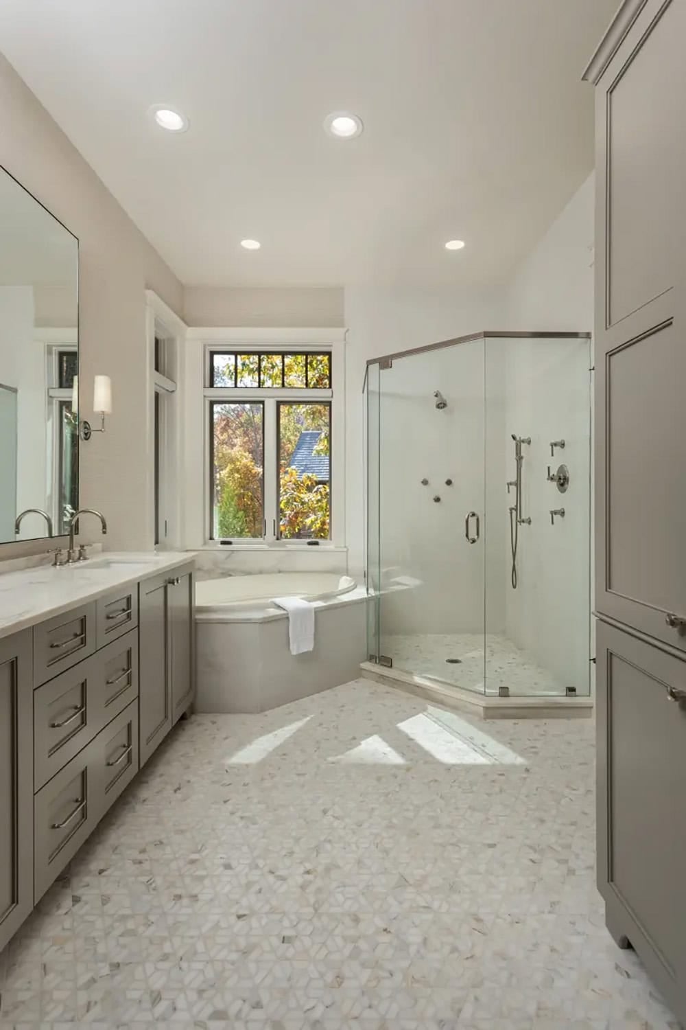 Primary ensuite bathroom with gray cabinetry, corner soaking tub, glass shower, and mosaic tile floor