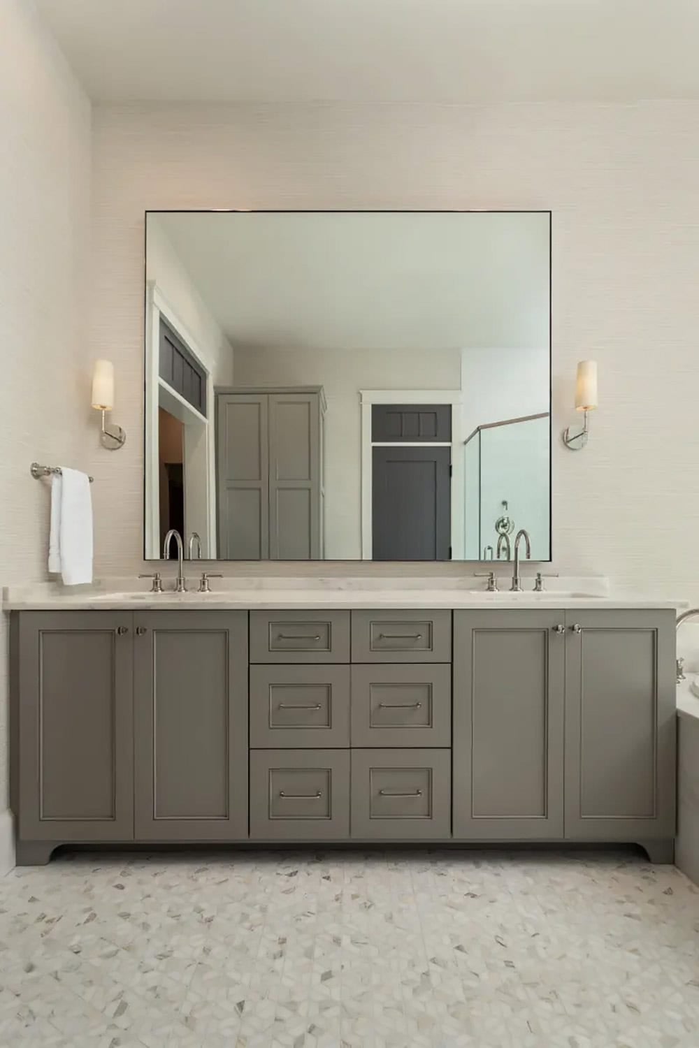 Double vanity bathroom with gray inset cabinetry, marble countertop, and large frameless mirror
