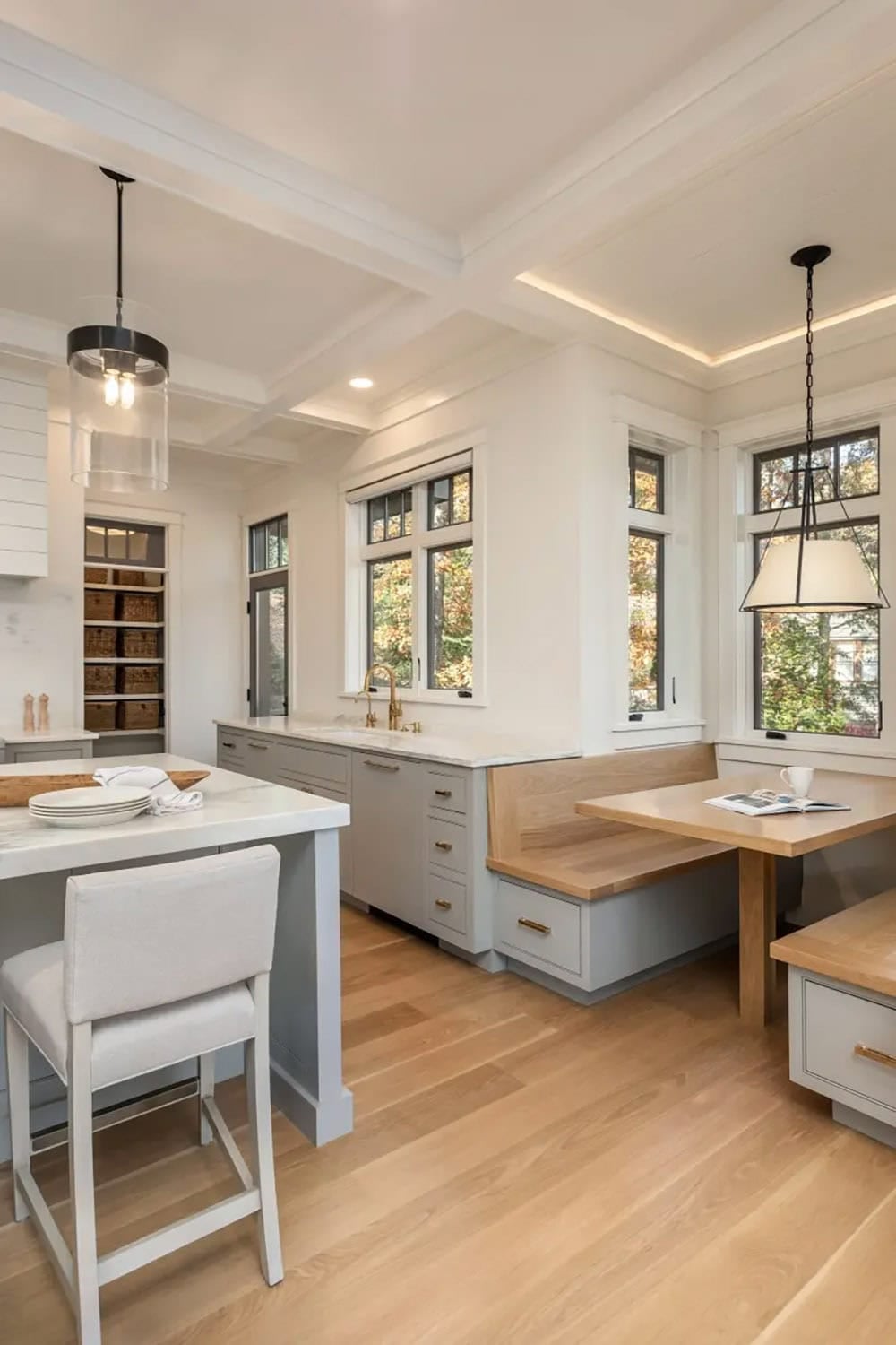 Kitchen nook with built-in bench seating, light wood table, coffered ceiling, and gold fixtures