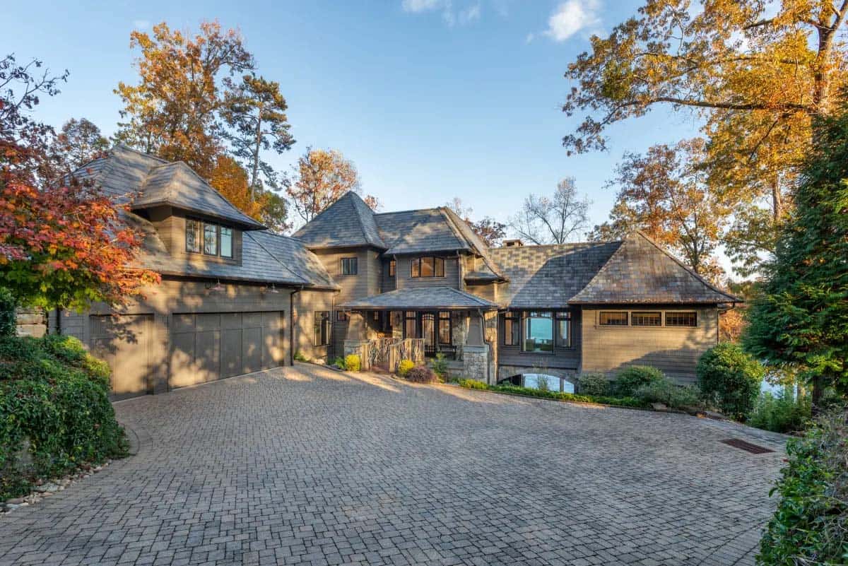 Front exterior of shingle-style lake house with slate roof, cobblestone driveway, and stone arch entry bridge