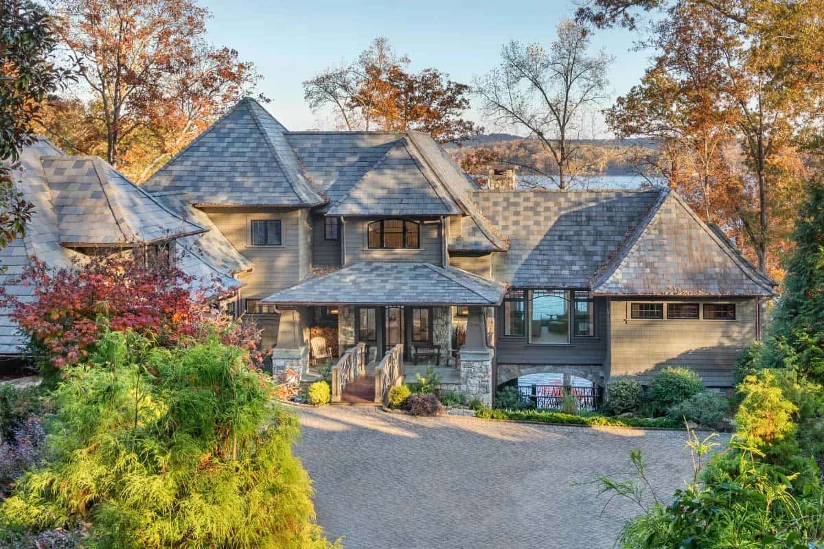 Aerial rear view of craftsman shingle lake house surrounded by colorful fall foliage with lake glimpse