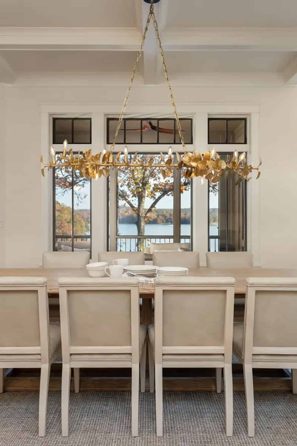 Formal dining room with gold botanical chandelier, upholstered chairs, and framed lake views beyond