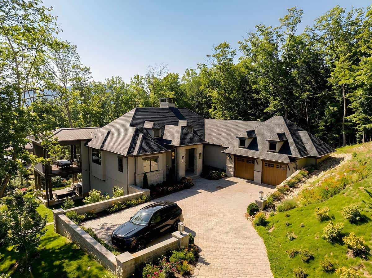 Aerial view of contemporary mountain home with dark hip roof, stone accents, and paver driveway nestled in Western North Carolina woodland