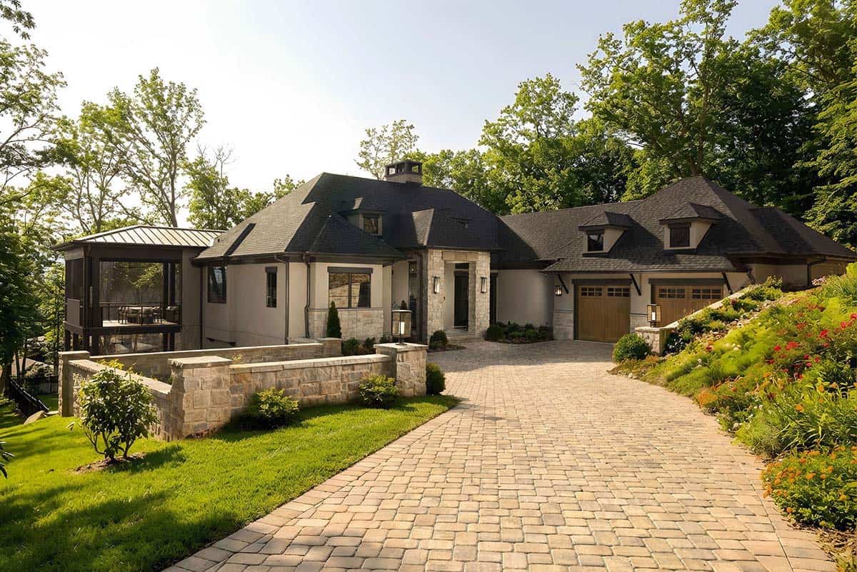 Contemporary stucco and stone mountain home with dark hip roof, screened porch, and paver driveway amid lush greenery