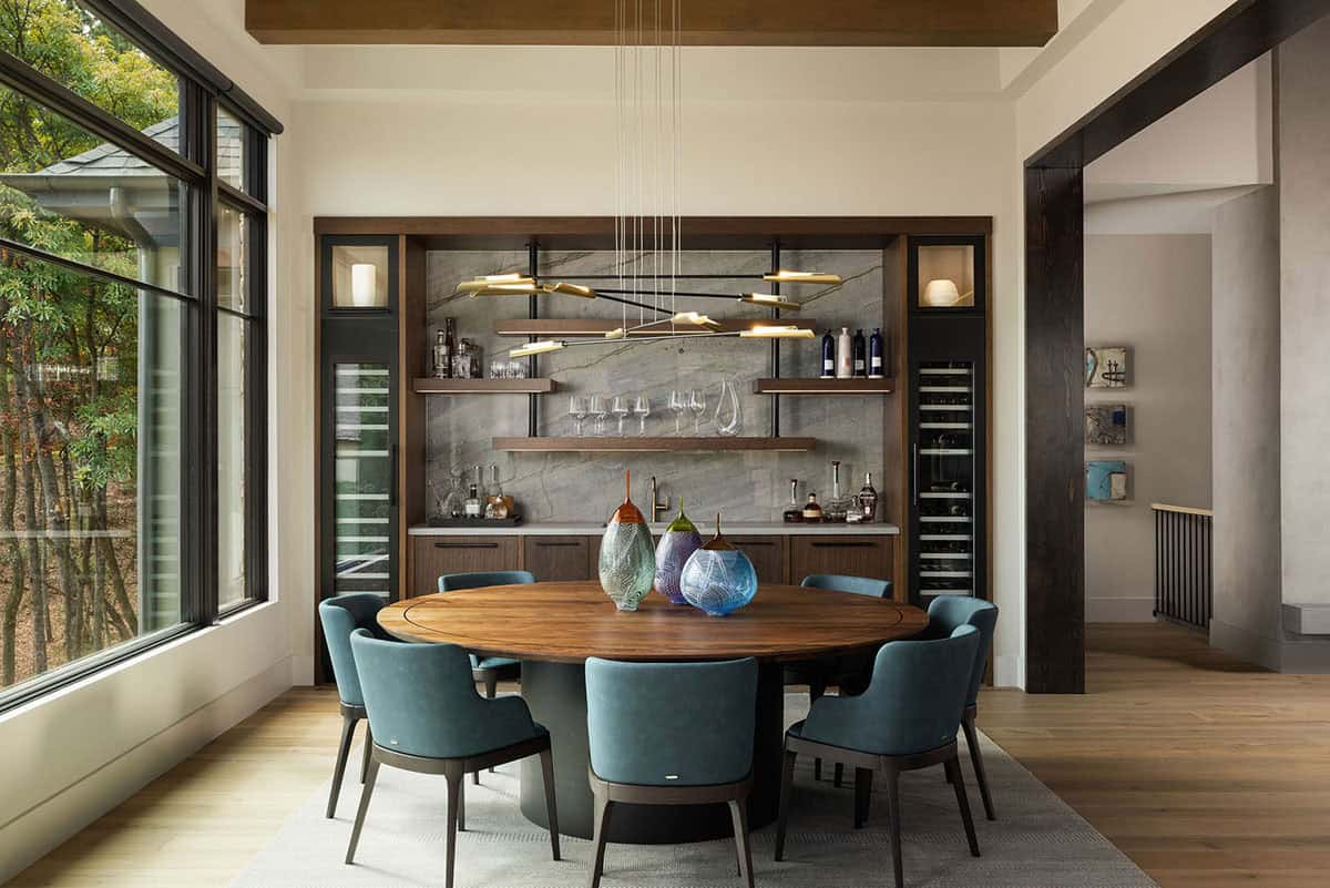 Dining room with locally crafted round walnut table, teal velvet chairs, quartzite cocktail bar, and wine columns