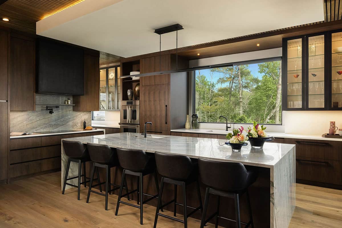 Dark walnut kitchen with quartzite waterfall island, black bar stools, stone backsplash, and large picture window with mountain views