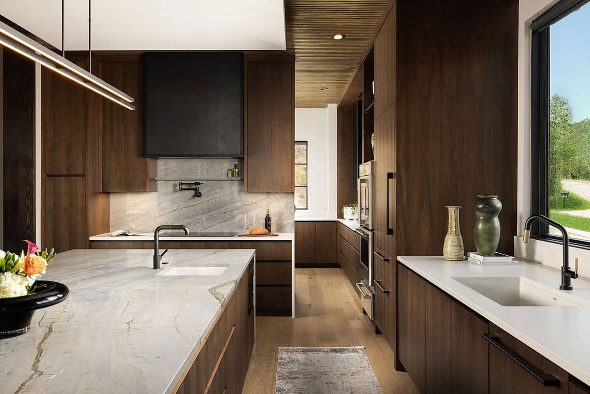 Kitchen detail showing dark walnut cabinetry, quartzite island, black steel range hood, and garden window with mountain views beyond