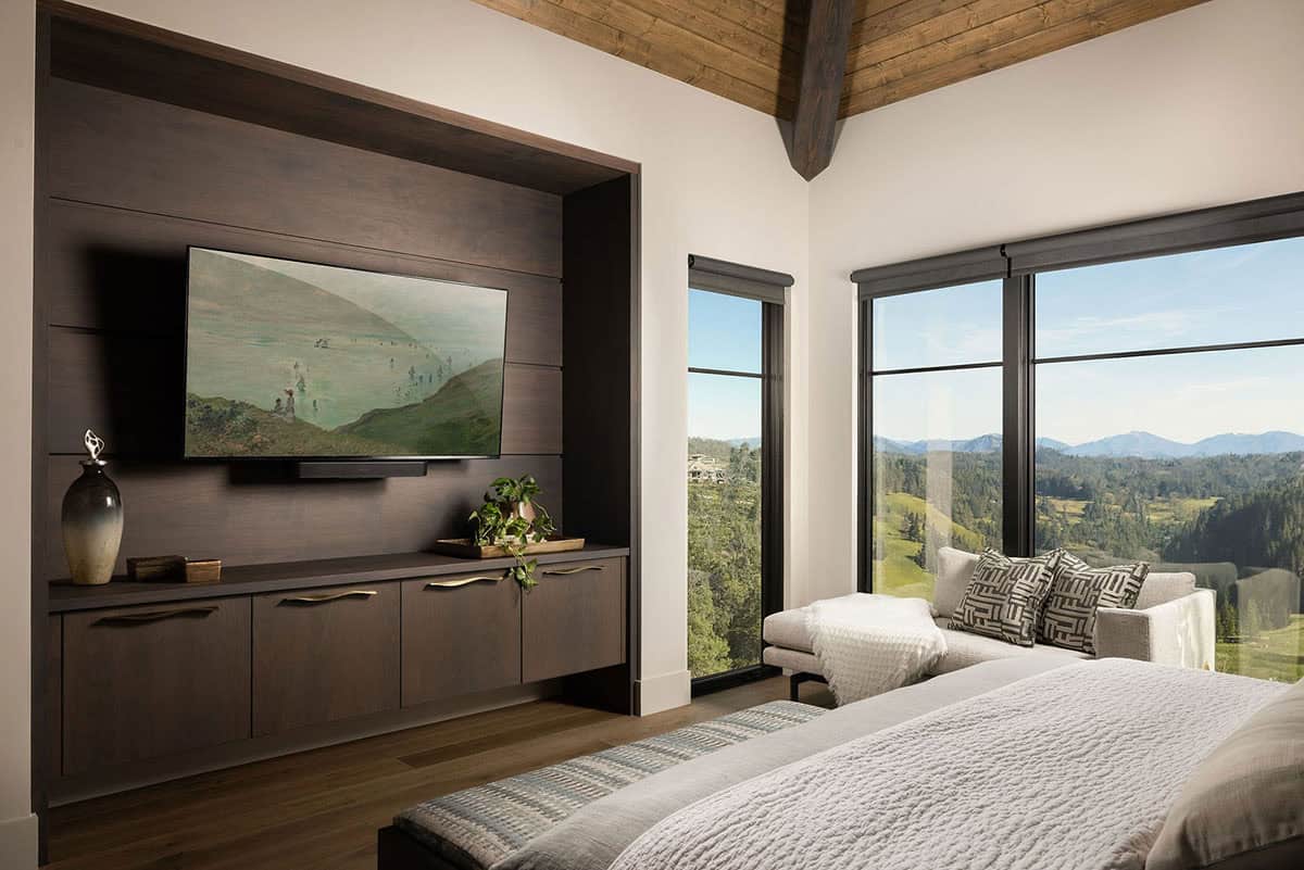 Primary bedroom with dark walnut built-in media wall, wood beam ceiling, and corner windows with sweeping mountain views