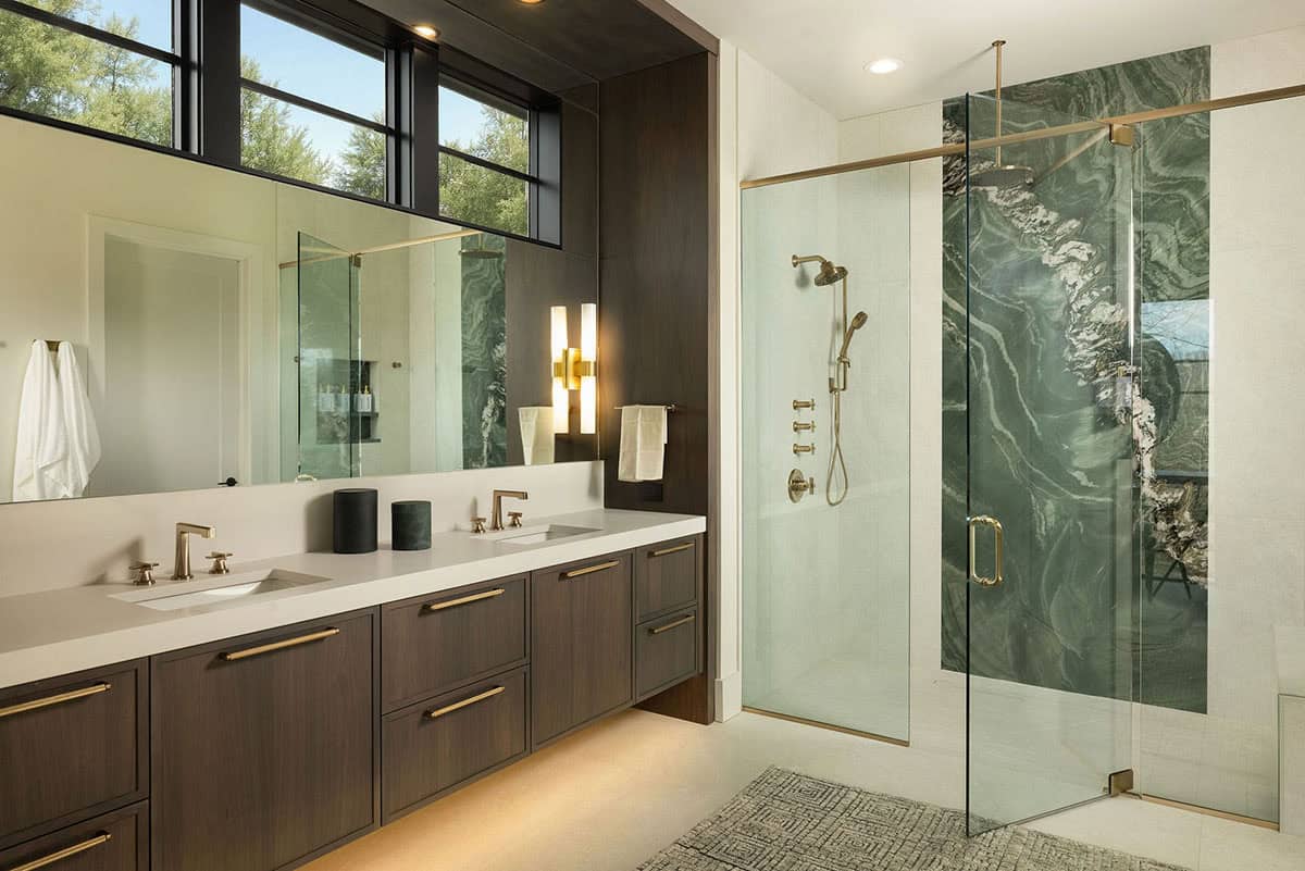Primary bathroom with dark walnut double vanity, white quartz countertop, brass fixtures, and dramatic green stone slab shower surround
