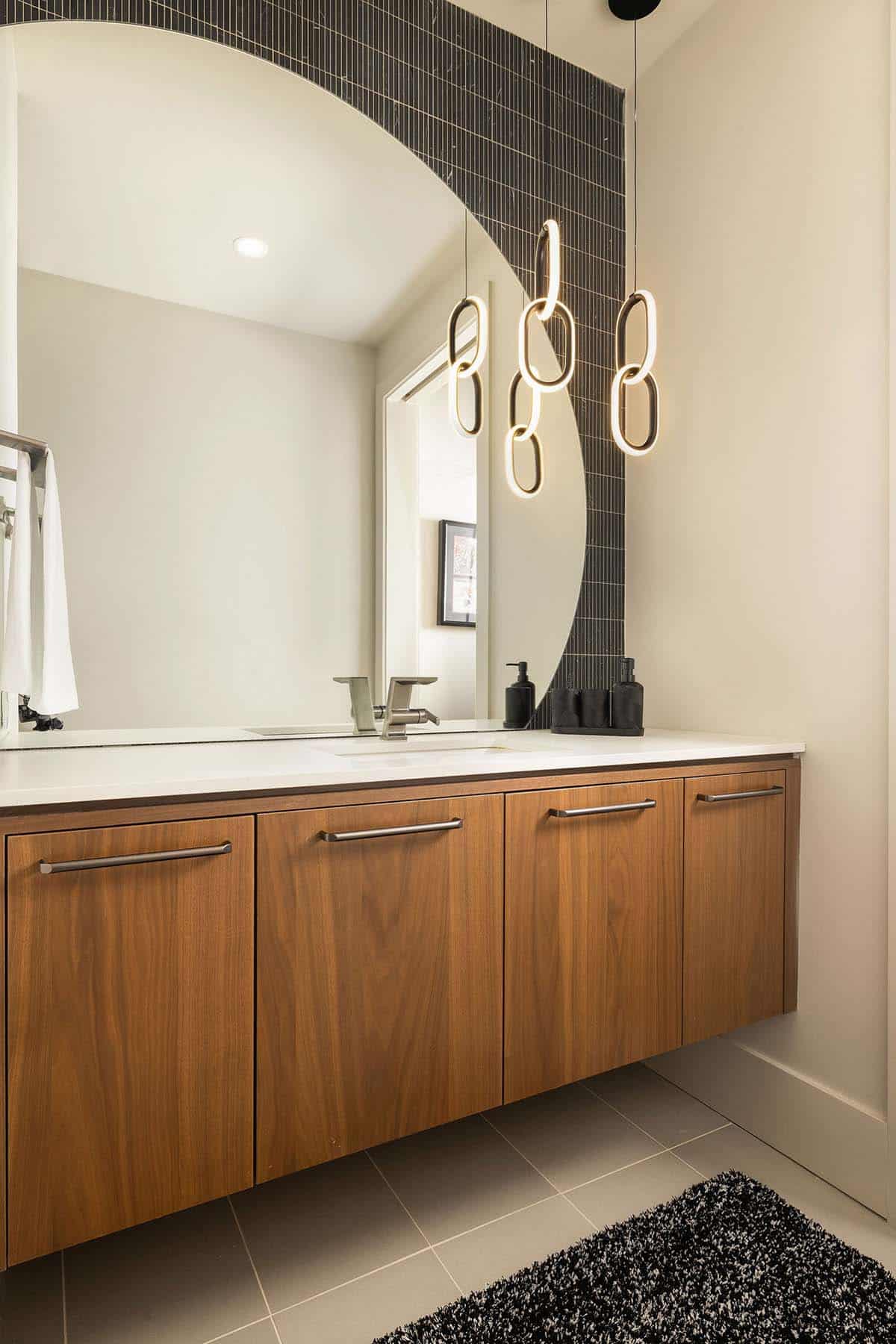 bathroom, floating vanity, walnut cabinetry, chain pendant light, dark tile accent wall, arched mirror