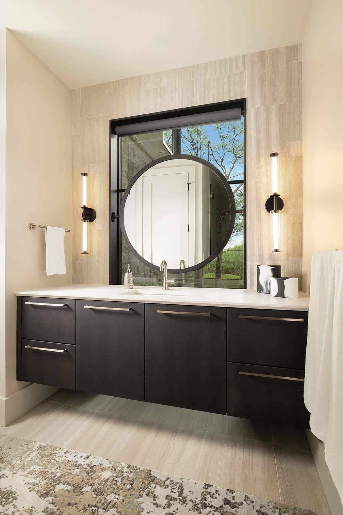 bathroom, dark floating vanity, round mirror, picture window, vertical sconces, stone tile