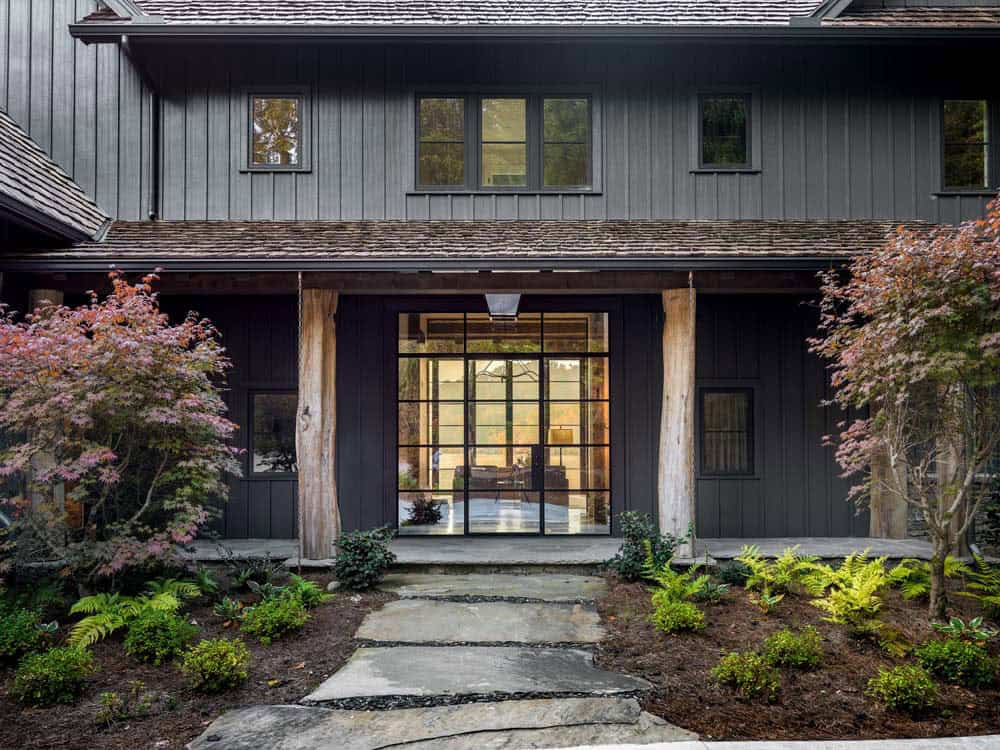 Dark exterior entrance with raw timber columns, steel-framed glass doors, and Japanese maples