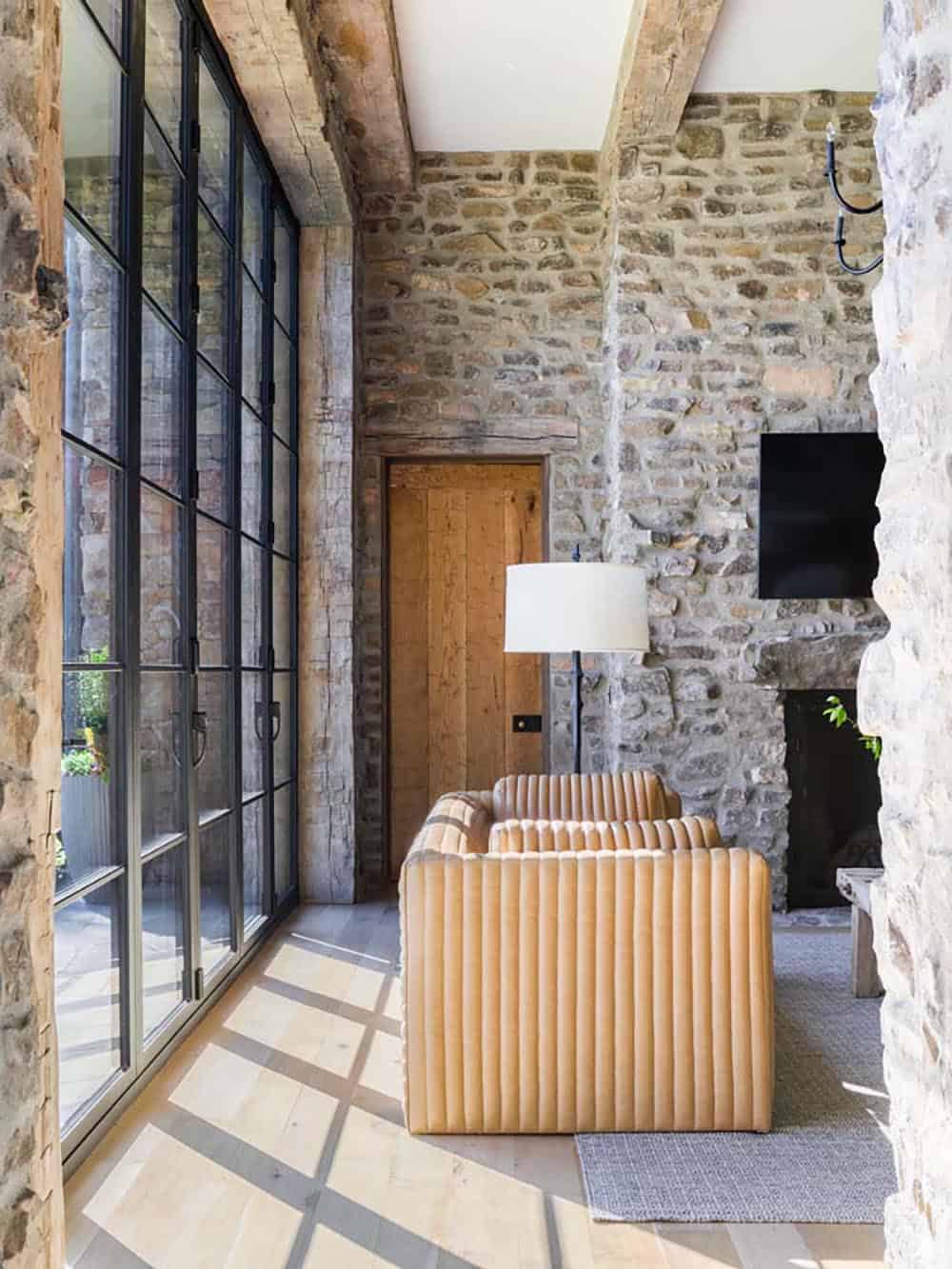 Stone wall sitting area with floor-to-ceiling steel-frame windows and channeled leather sofa