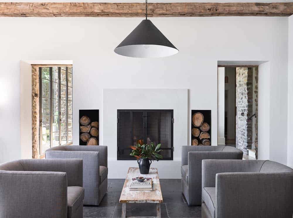 Minimalist white living room with fireplace, log storage niches, and exposed beam ceiling