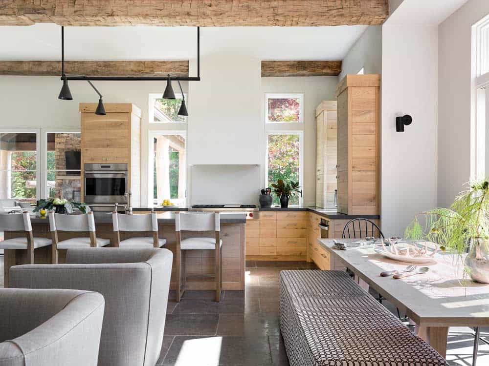 Open-plan kitchen and dining with light oak cabinets, reclaimed beams, and black pendant lights