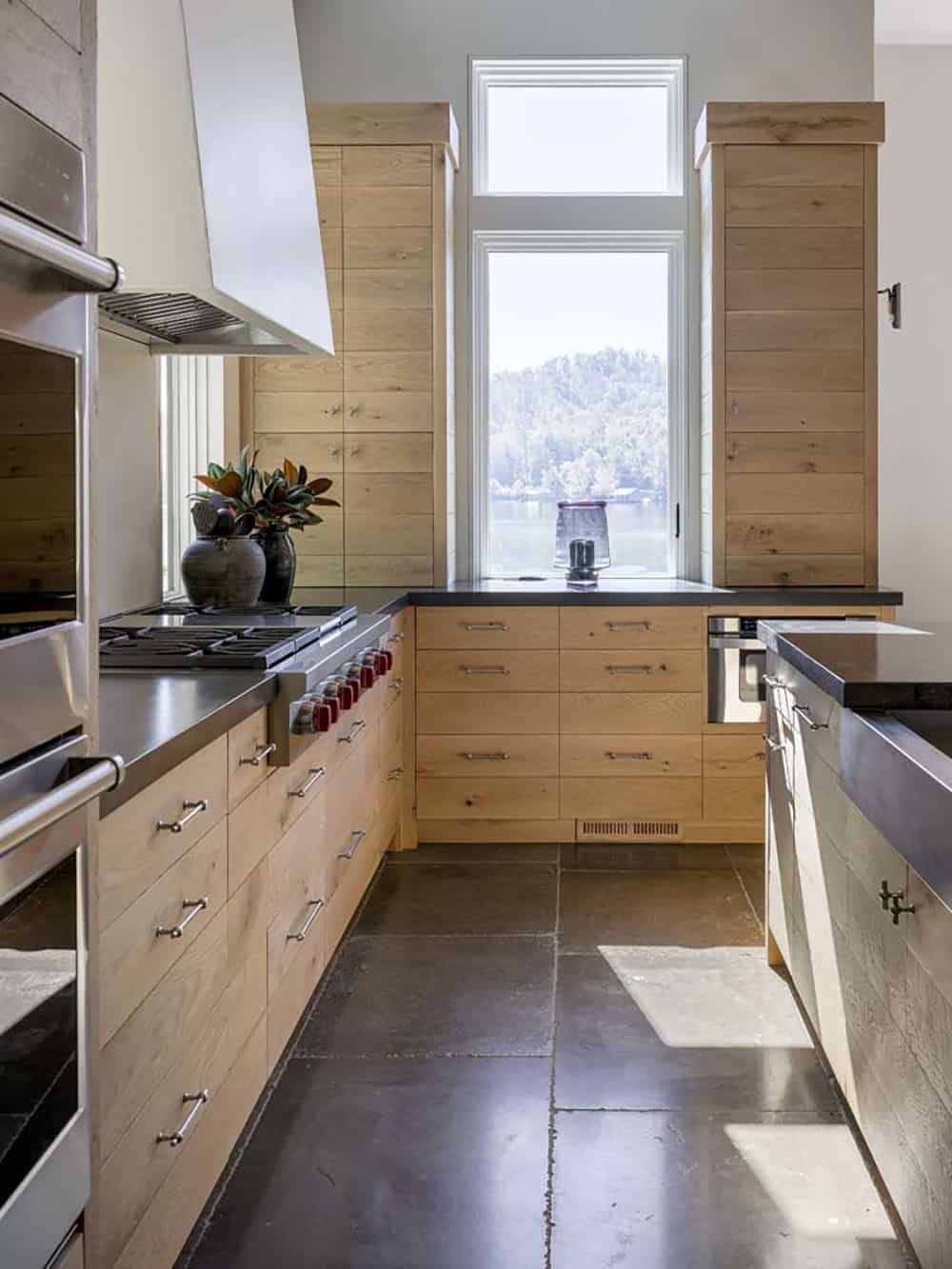 Kitchen galley with light oak cabinetry, dark stone countertops, and lake window view