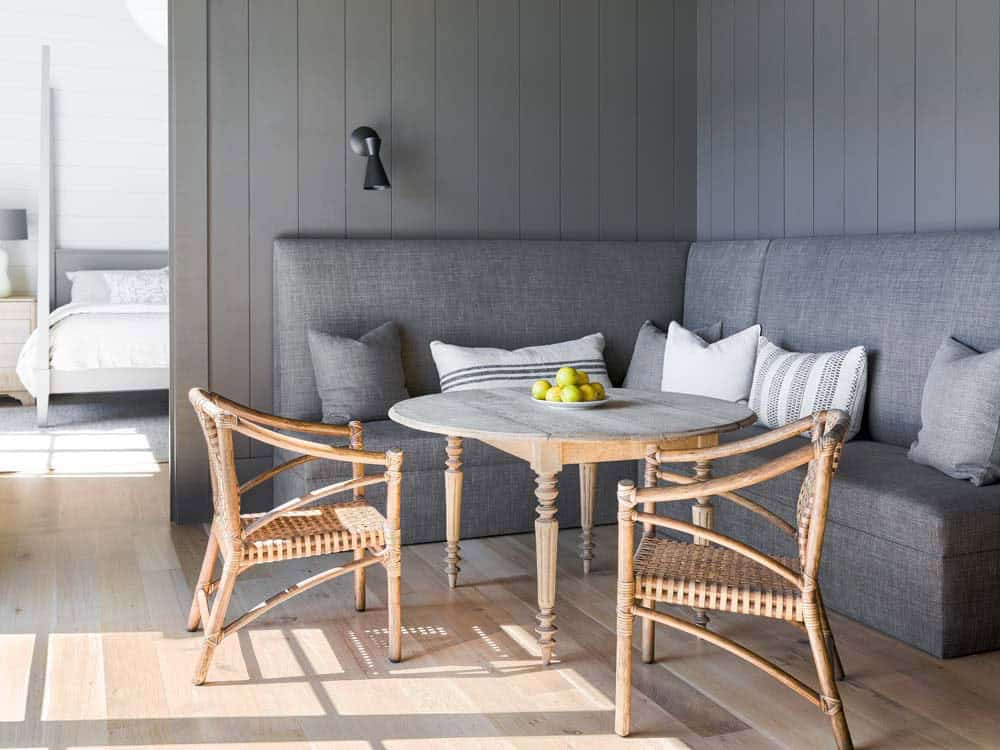 Built-in banquette with gray upholstery and rattan chairs beside primary bedroom