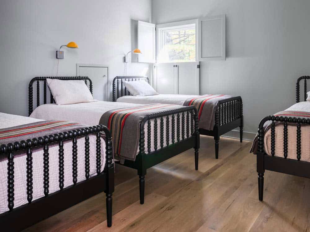 Bunk room with four black spindle twin beds and orange wall sconces