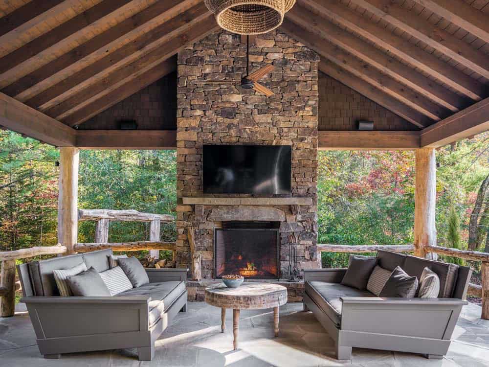 Covered outdoor pavilion with stone fireplace, wood-beam cathedral ceiling, and gray patio sofas