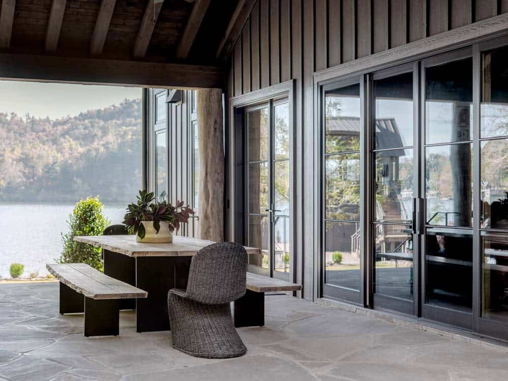 Covered lakeside porch with reclaimed wood dining table, benches, and steel-frame folding doors