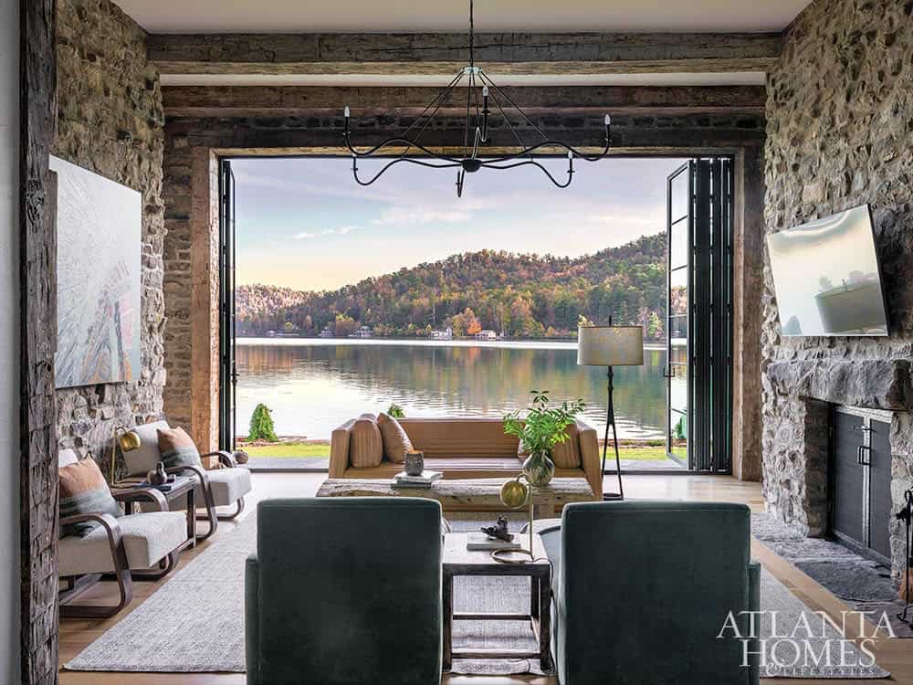 Stone-walled living room with open bifold doors revealing panoramic autumn lake view at dusk