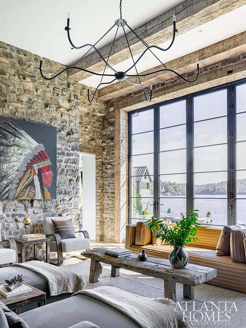 Stone-walled living room with reclaimed beam ceiling, sculptural chandelier, and lake-view windows