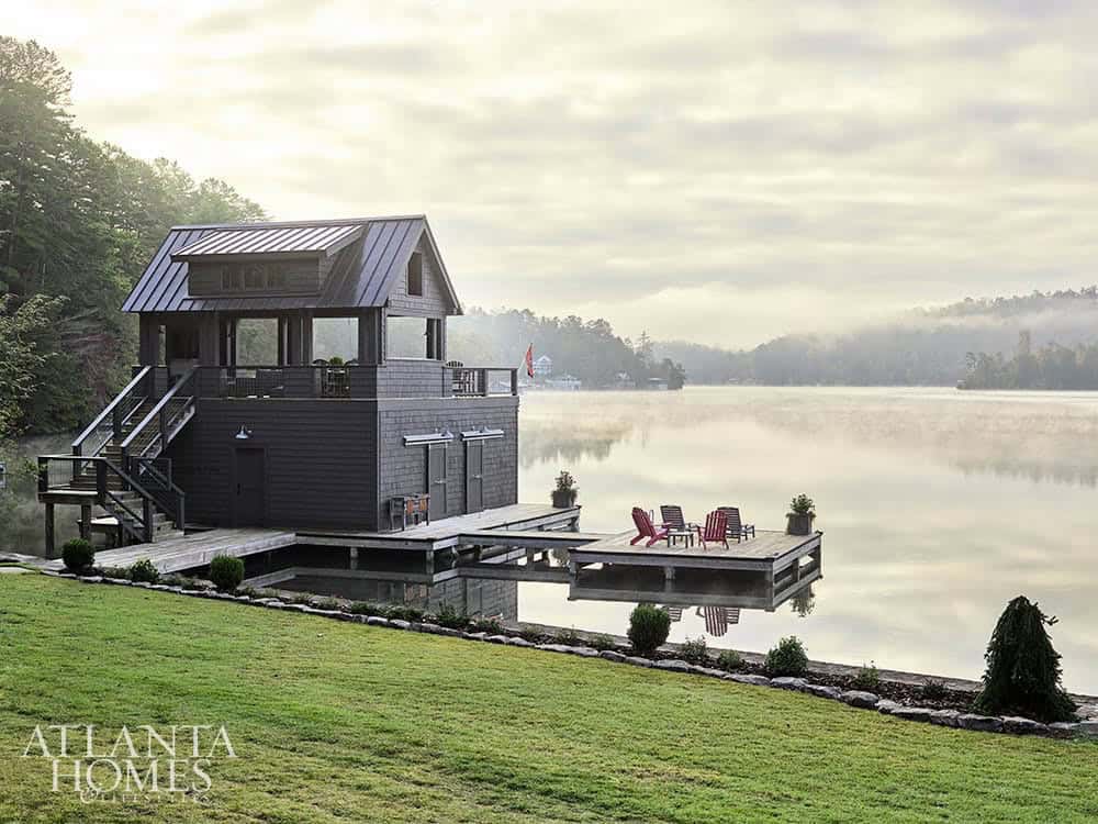 Gray shingle boathouse with metal roof, upper deck, and red Adirondack chairs on misty morning lake