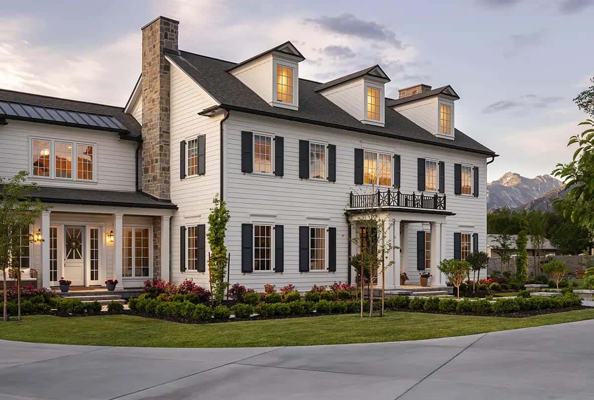 Colonial home exterior at dusk with black shutters, stone chimney, and mountain views