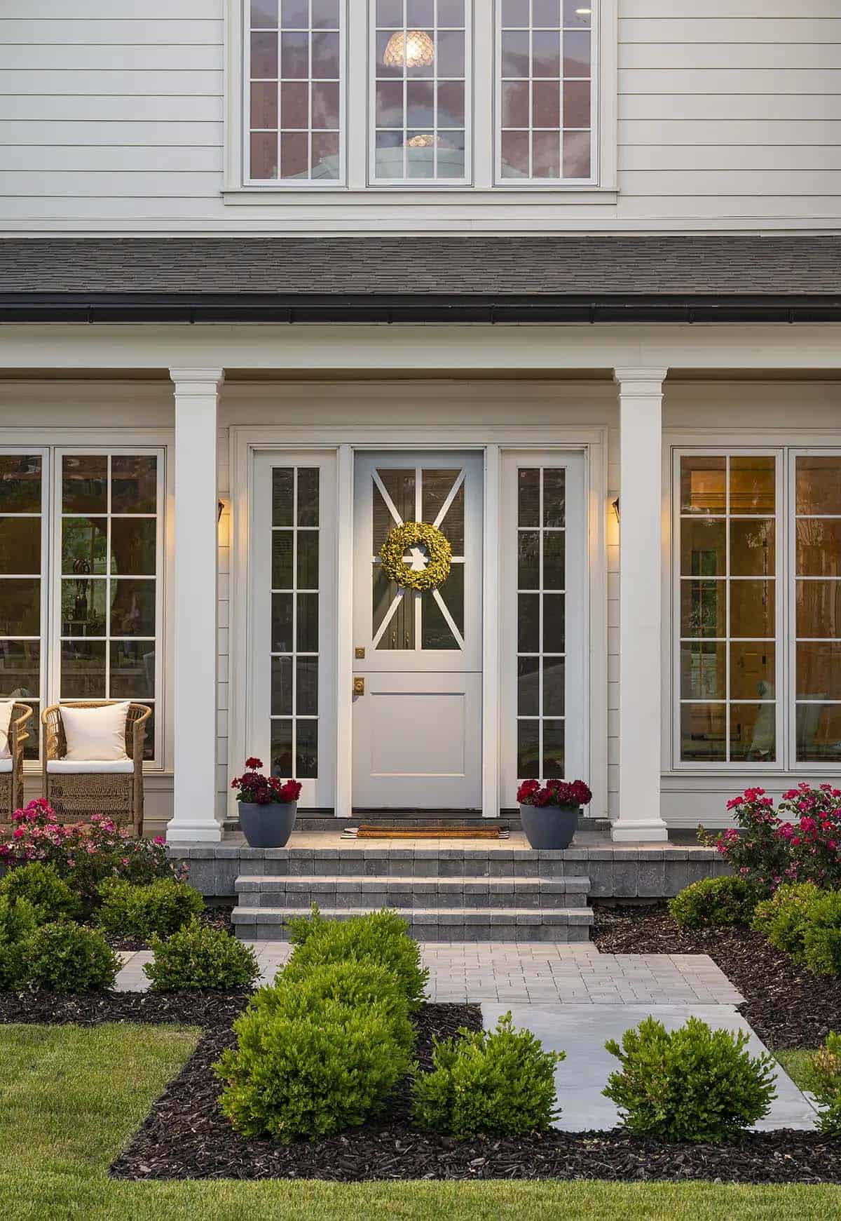White front door with wreath, flanking sidelights, columns, and boxwood landscaping