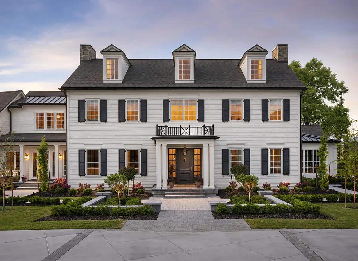 Colonial home facade at twilight with black door, Juliette balcony, and dormer windows