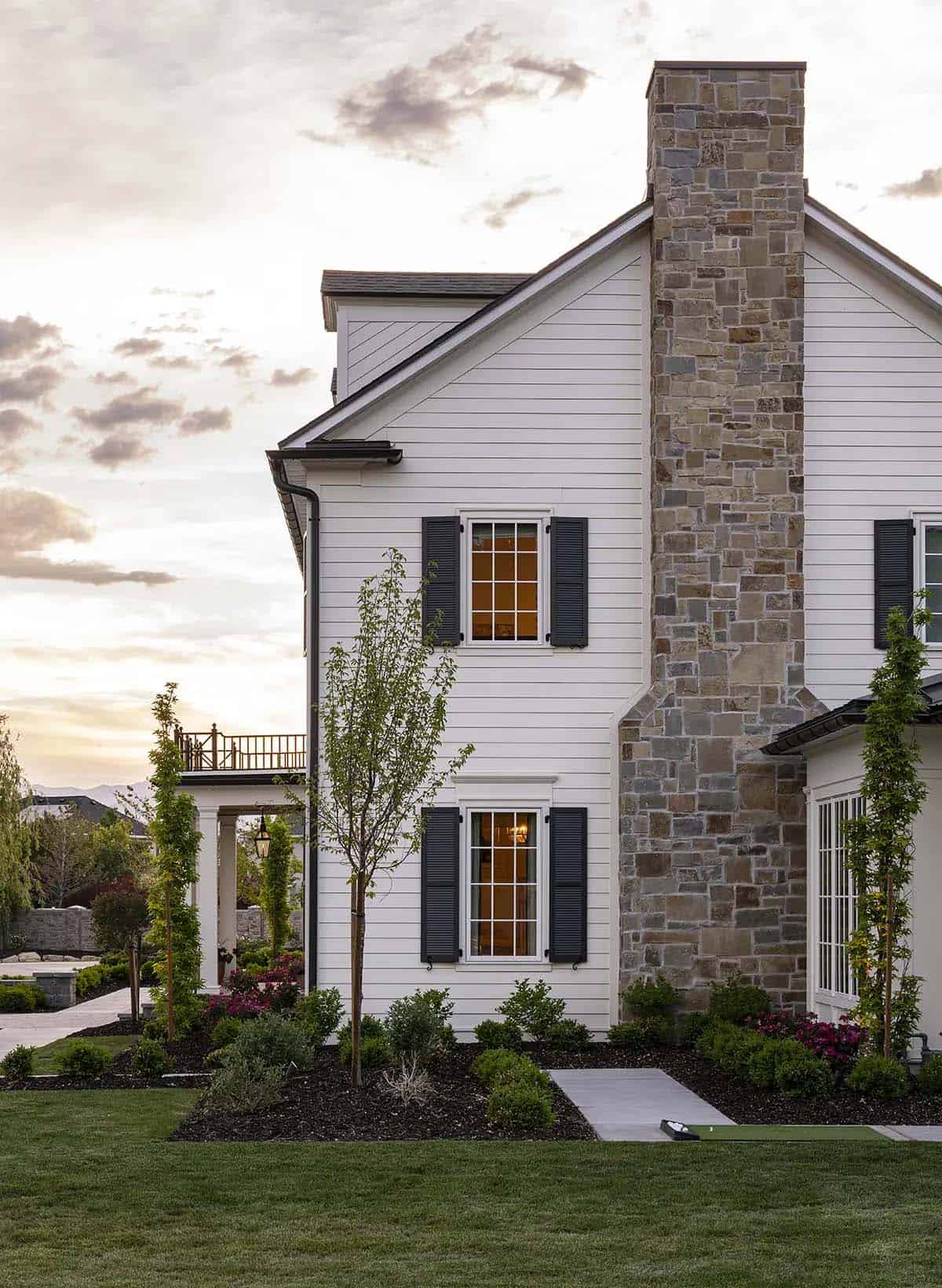 White colonial home side exterior with stone chimney and black shutters at sunset