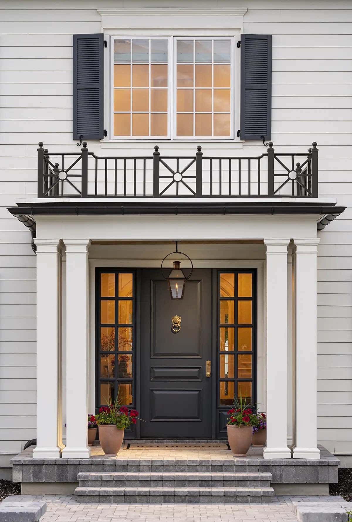 Black front door with brass lion knocker, sidelights, columns, and iron Juliette balcony