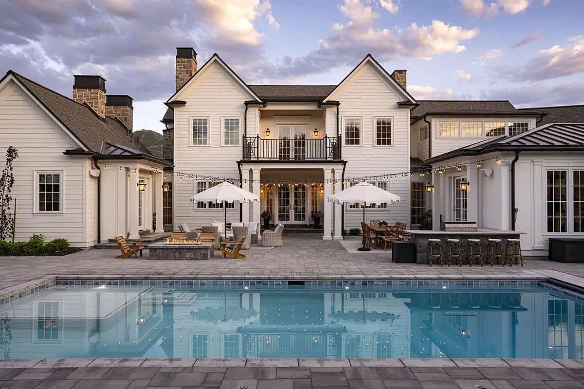 Colonial home backyard at dusk with pool, fire pit, outdoor bar, and string lights