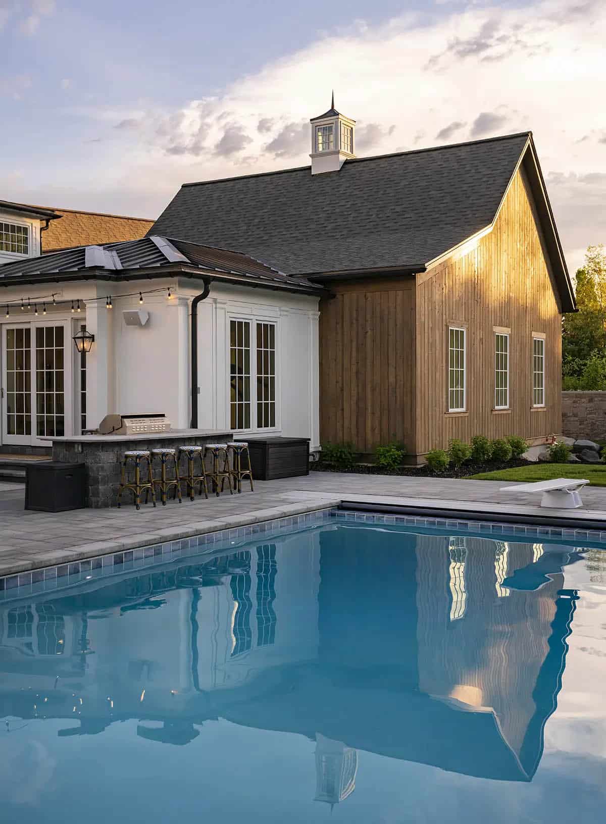 Pool house with cedar siding, cupola, outdoor kitchen, and bar seating at sunset