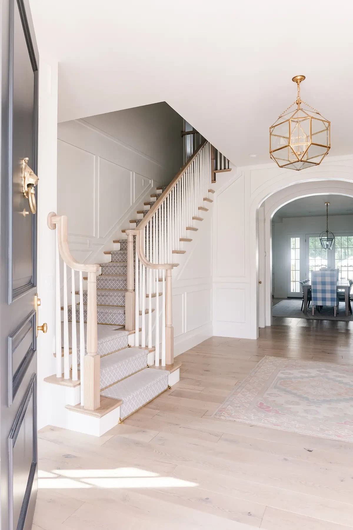 Foyer with curved staircase, patterned carpet runner, wainscoting, and gold pendant light