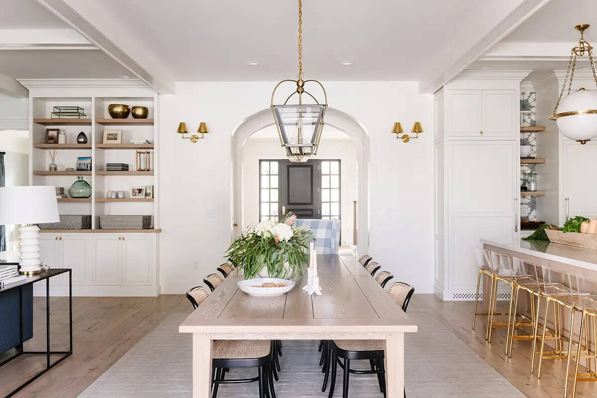 Open dining room with long wood table, cane chairs, built-in shelves, and arched doorway