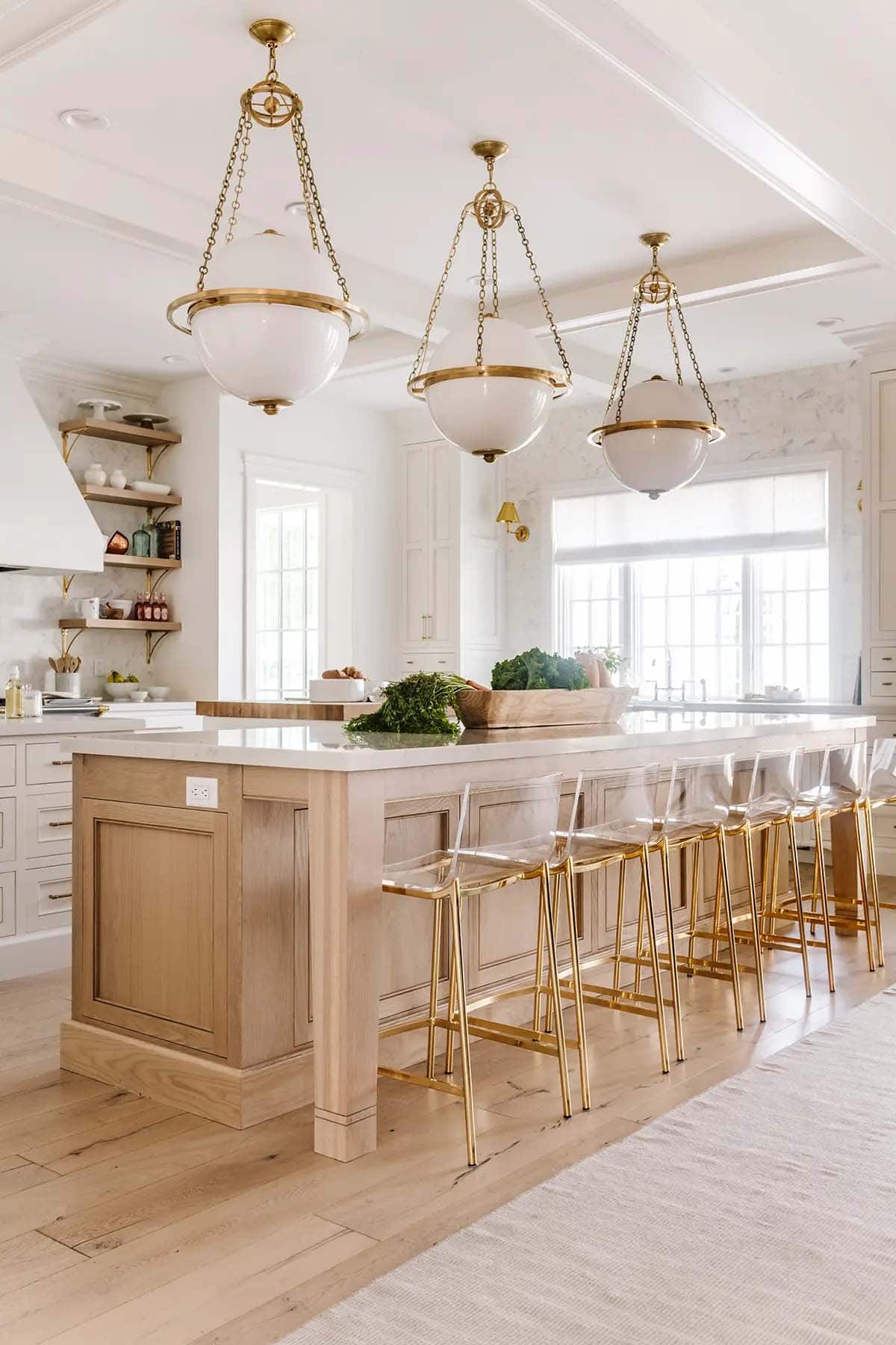 White kitchen with large wood island, acrylic gold bar stools, and globe pendant lights