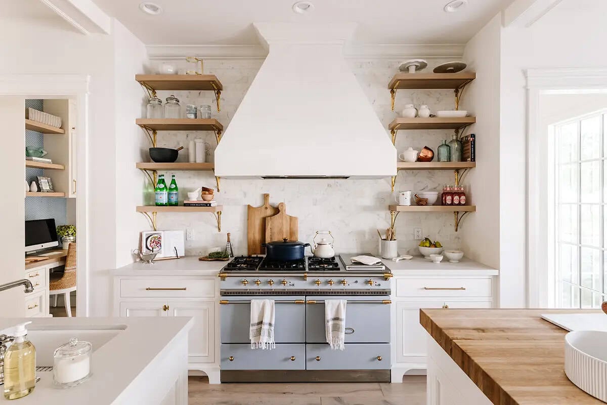 White kitchen with blue La Cornue range, plaster hood, open shelving, and marble backsplash