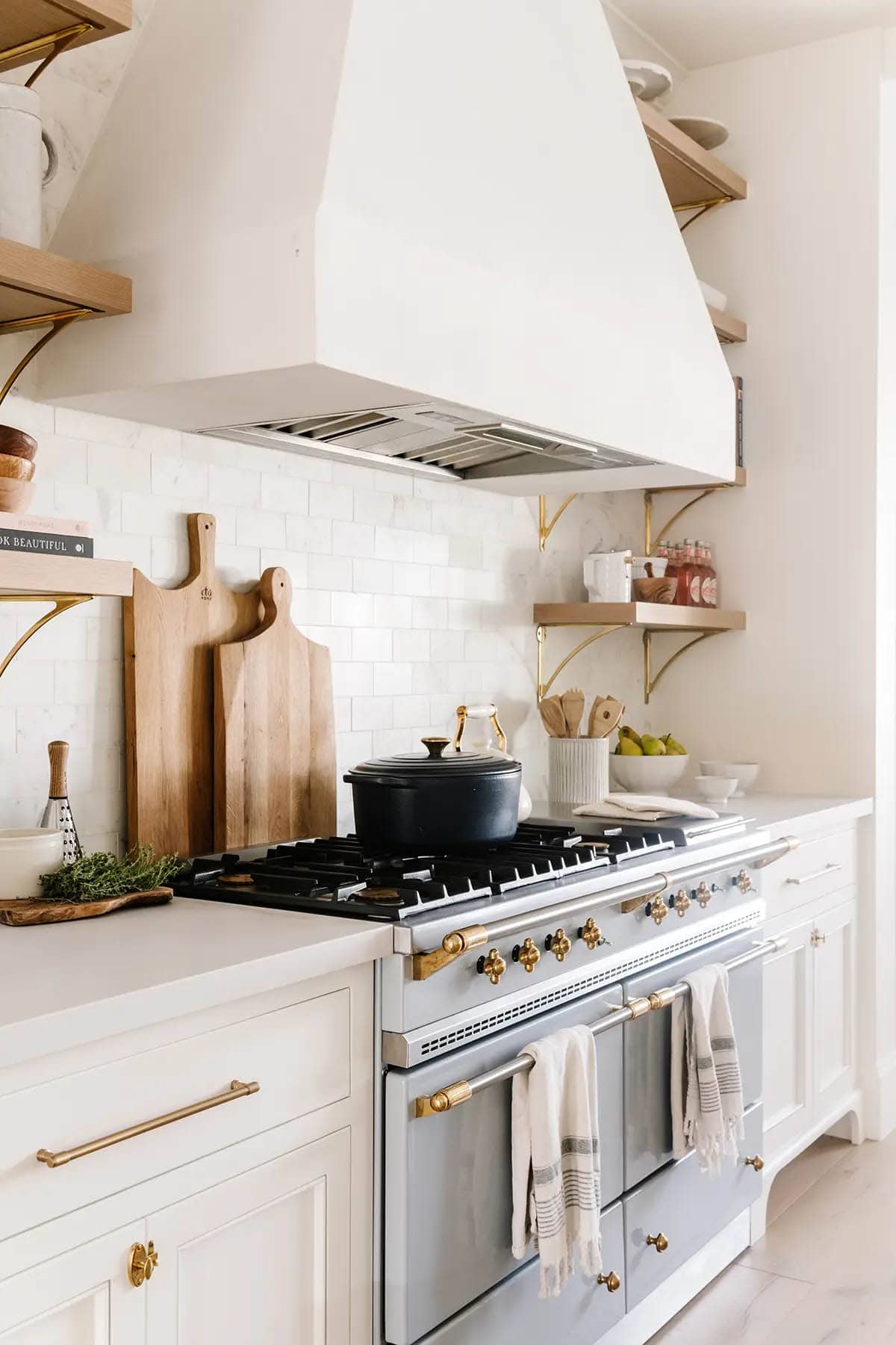 Close-up of blue La Cornue range with brass fittings, plaster hood, and wood cutting boards