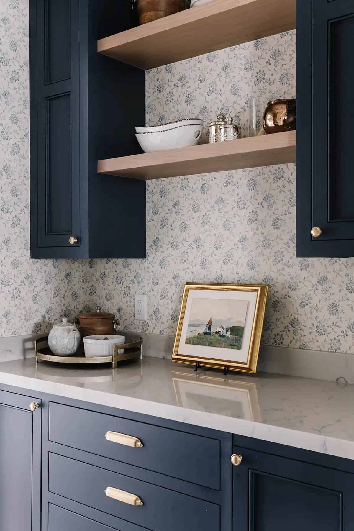 Navy blue butler's pantry with floral wallpaper, open shelving, and brass hardware