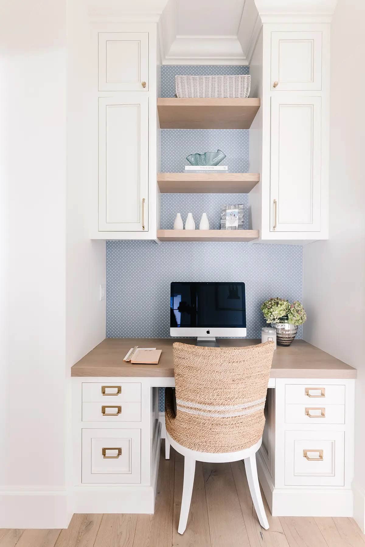 Built-in kitchen desk nook with blue polka dot wallpaper, open shelving, and wicker chair