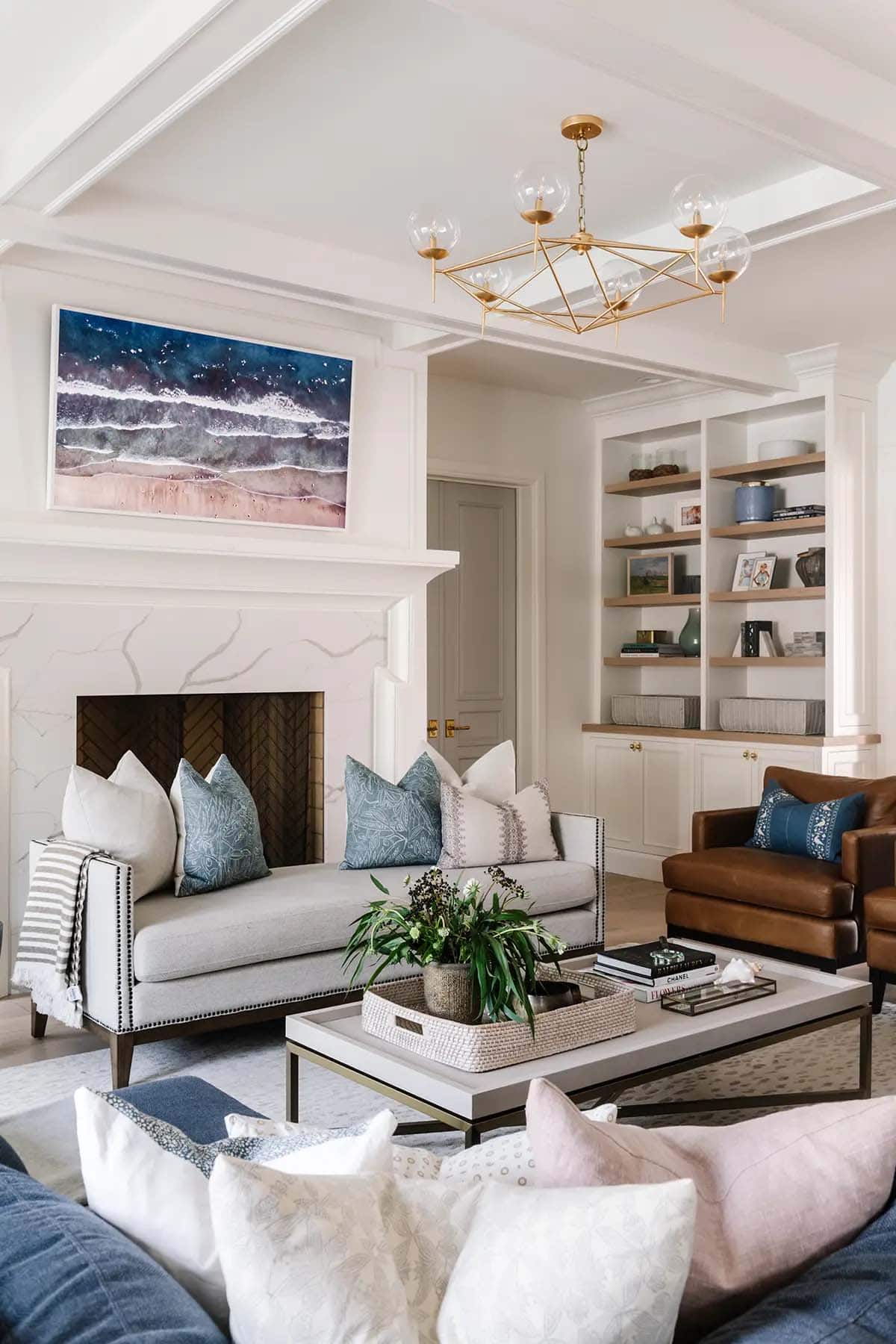 Living room with marble fireplace, built-in shelves, blue pillows, and gold globe chandelier