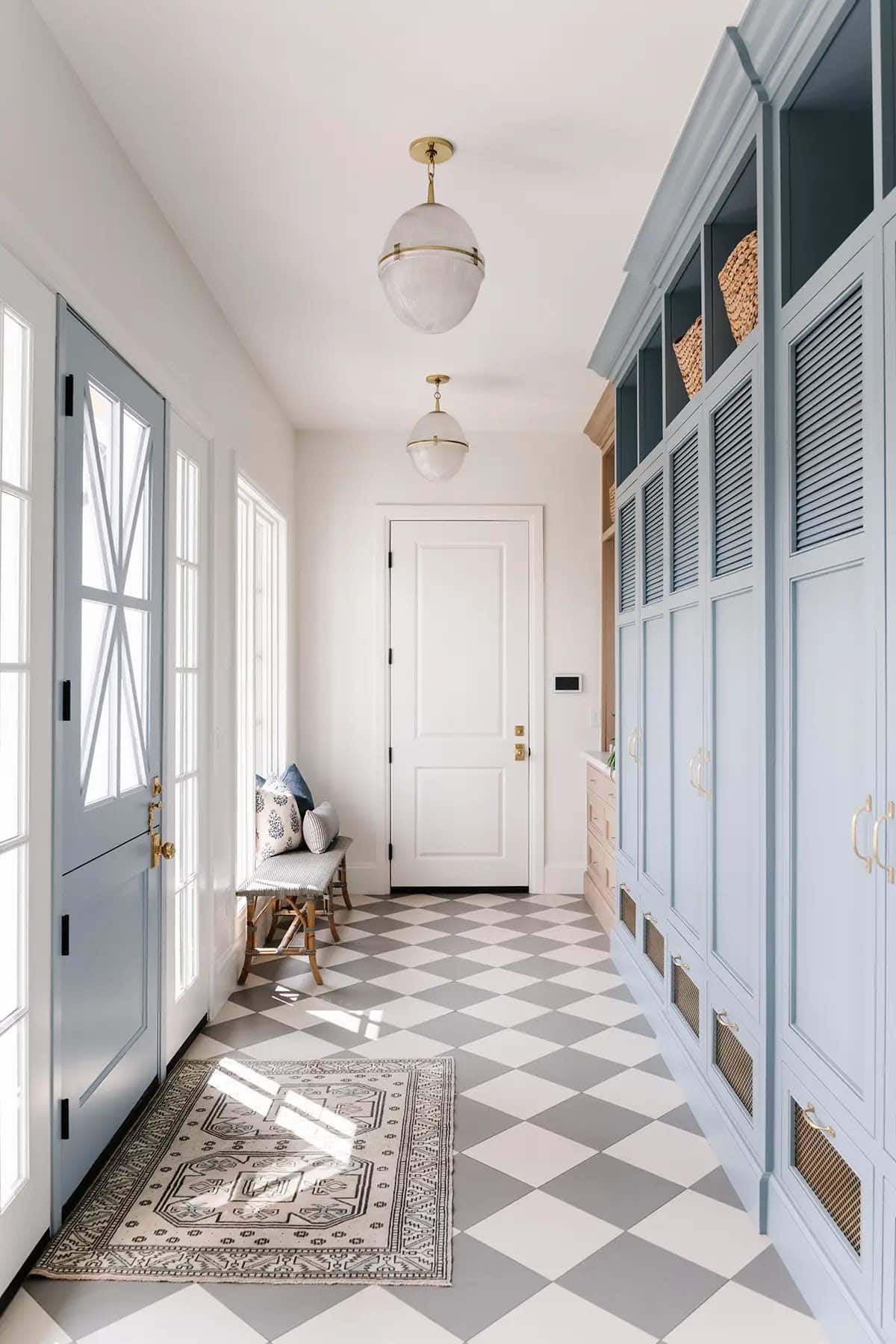 Blue mudroom with checkered floor, globe pendants, louvered cabinets, and brass hardware